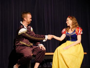 Two actors shaking hands in costumes on stage.