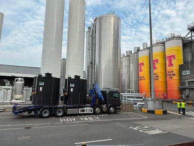 A truck parked near large industrial tanks at a factory site.