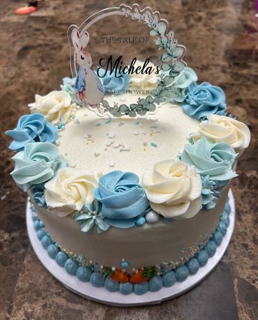 A beautifully decorated baby shower cake with blue and white rose frosting and a cute bunny topper.