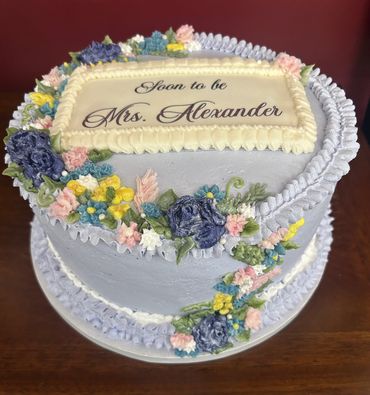 A beautifully decorated engagement cake with floral designs and the message 'Soon to be Mrs. Alexander'.