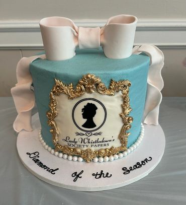 Elegant blue cake with white bow and gold frame, themed 'Lady Whistledown'.