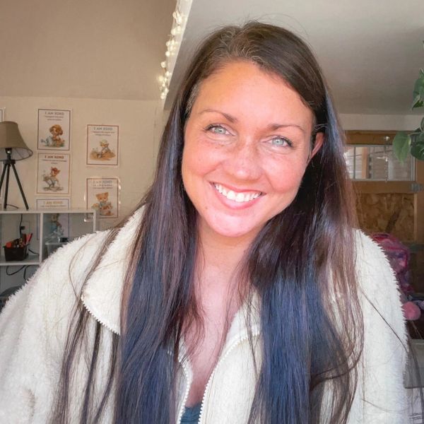 Smiling woman with long dark hair in cozy cream jacket indoors.