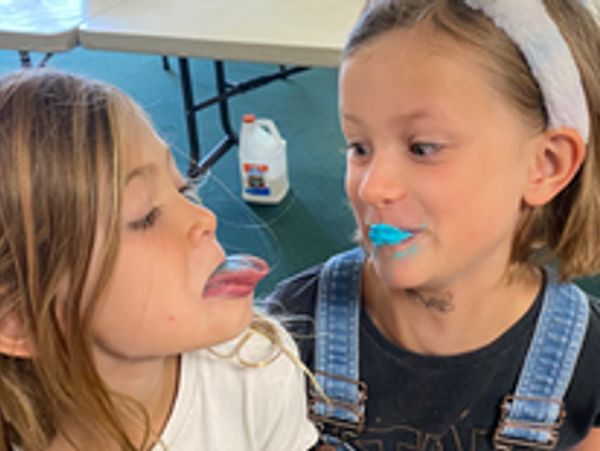 Two girls playfully interacting with colorful frosting.