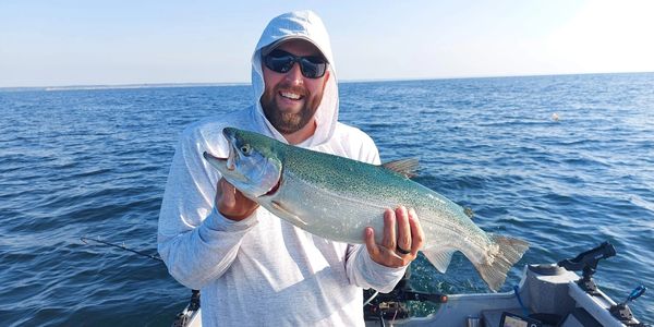 Man in hoodie holding a large fish on a boat in open water.