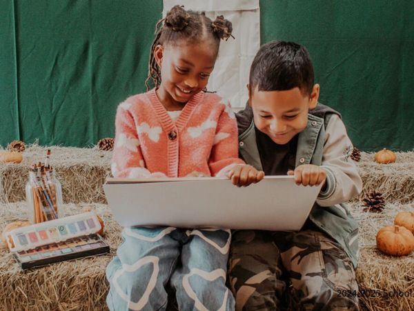 Two students doing art together while sitting on fall themed straw bales