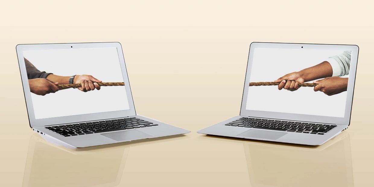 Two laptops with hands on screen playing tug-of-war with a rope.