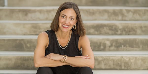 Smiling woman sitting on outdoor steps, wearing black sleeveless top and jewelry.