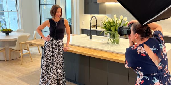 A woman posing for a photo shoot in a modern kitchen with a photographer taking pictures.