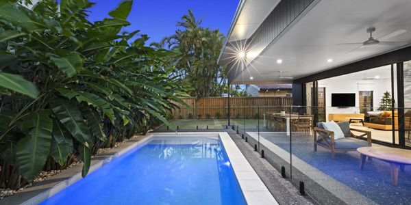 Modern backyard with a swimming pool, glass fence, and outdoor seating area.