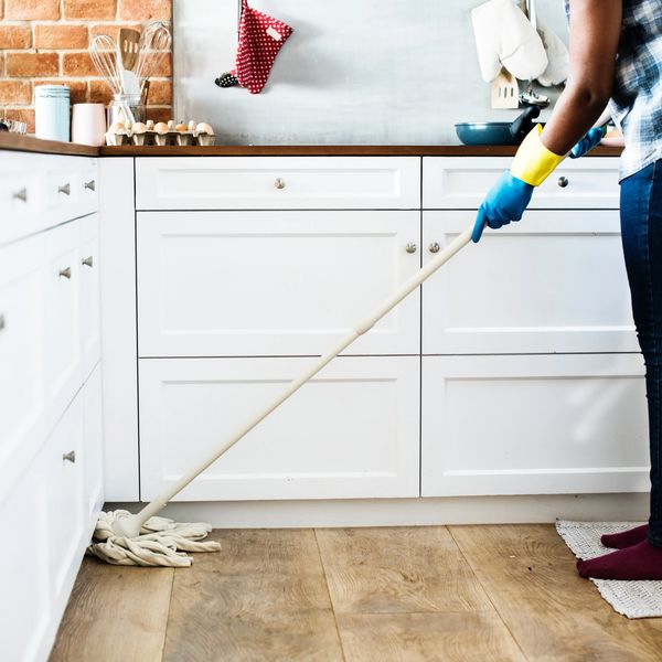 Person mopping kitchen floor wearing gloves.