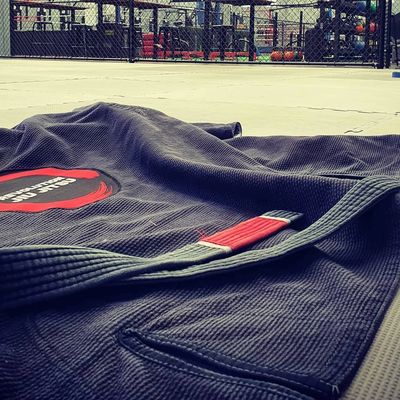 Jiu Jitsu Gi and Black Belt layed out on mats below Revolution Jiu Jitsu Sign