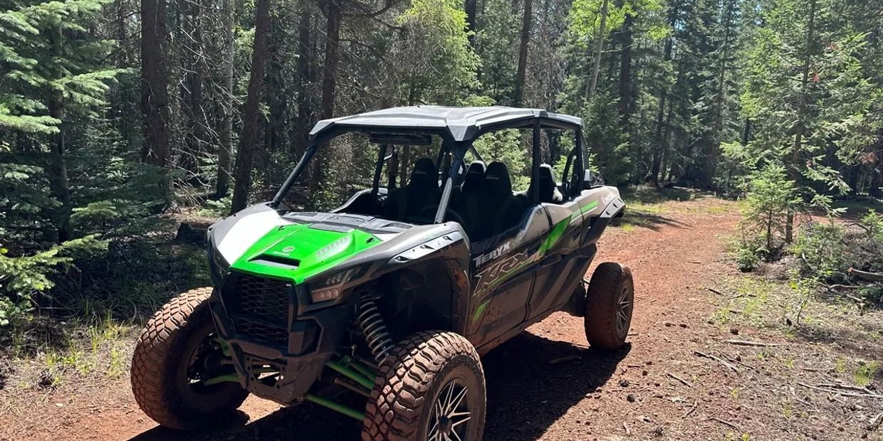 A green and black off-road vehicle on a dirt path in a forest.