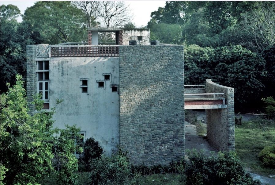 Modern concrete and stone house surrounded by trees.
