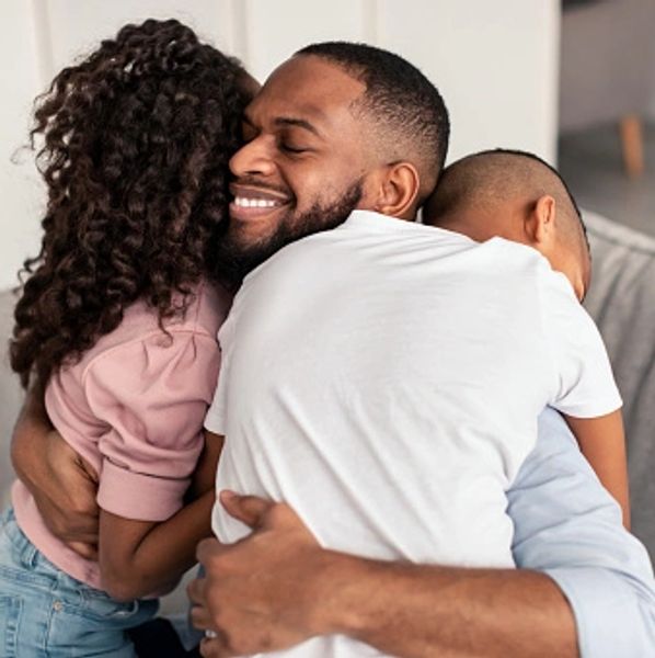 A man hugging his two kids in his house sitting on the sofa