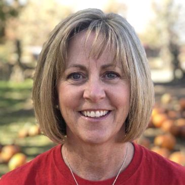 Smiling woman outdoors with pumpkins in the background.