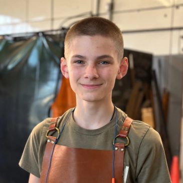 Young person smiling wearing a brown apron.