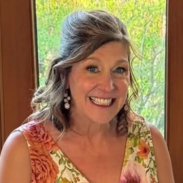 Smiling woman in floral dress with pearl earrings.
