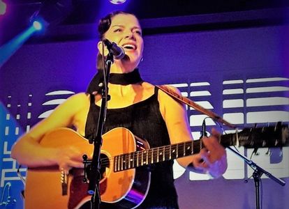 Woman singing and playing guitar on stage.
