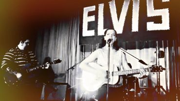 Two musicians perform under a sign reading ELVIS.