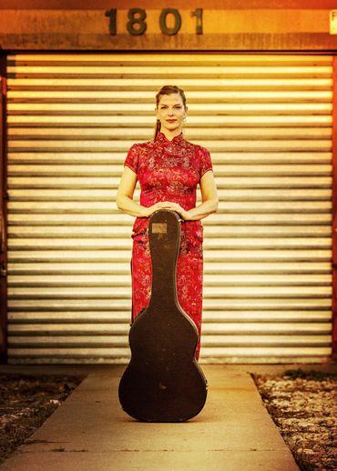 Woman in red dress holding a guitar case.