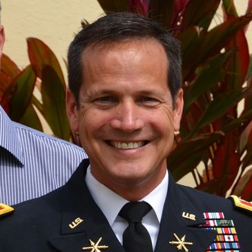 Smiling military officer in dress uniform with medals and ribbons.