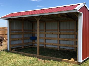 Red and white open-sided animal shelter on grass.
