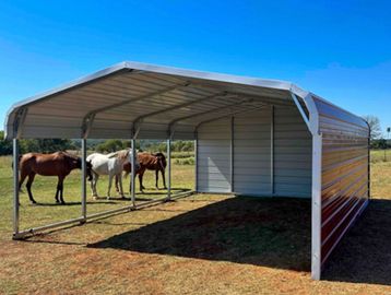 Metal shelter with horses standing under it in a field.