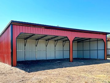 Red metal barn sheds with open fronts on a dirt ground.