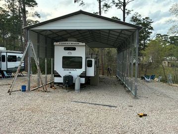 RV parked under a large metal carport in a gravel area.