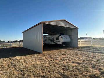 RV parked inside a metal shelter in a dry field.