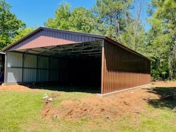 Brown metal shed with an open front in a grassy area.