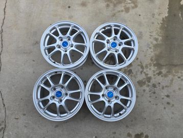 Four silver alloy car wheels with blue center caps placed on concrete.