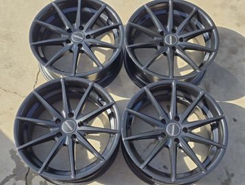Set of four black multi-spoke car rims on the ground.