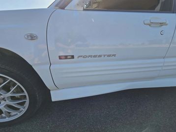 Close-up of a white Subaru Forester's side with a visible badge and wheel.