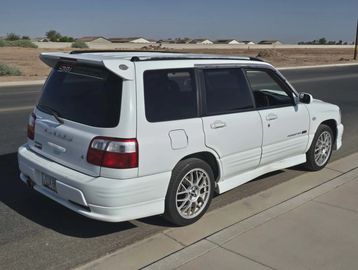 White Subaru Forester parked on the street with sporty wheels.