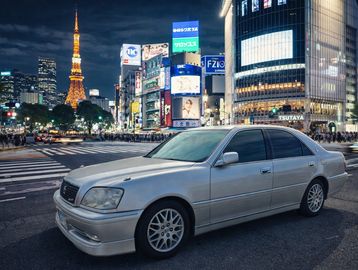 A silver luxury sedan parked at a busy city intersection at night.