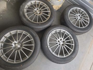 Four alloy car wheels with tires arranged on a floor.