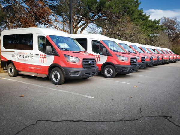 A lineup of wrapped Mid Cumberland public transit vans parked outdoors in a row.