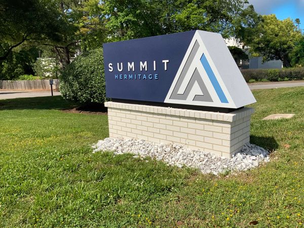 Outdoor monument sign for Summit Hermitage on a sunny day with green grass and trees.