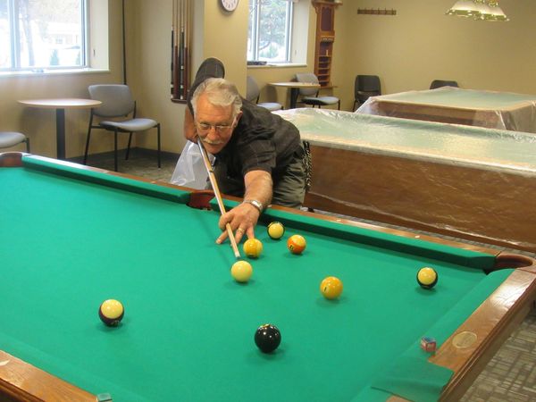 Member shoots pool, aiming cue at cue ball to hit 8 Ball