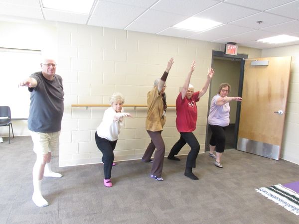 4 Modified Yoga participants in a warrior pose using the wall for support, with instructor at ARC