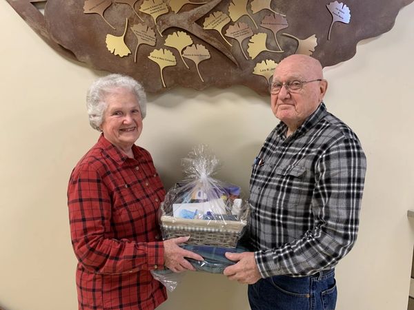 Evie & Louis McCain stand under ARC Giving Tree each holding one end of Sunshine Program basket