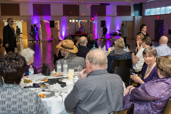 Group of people seated at tables facing DJ at senior prom in ARC Rec Room