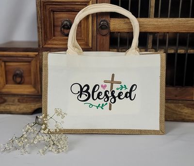 A beige tote bag with "Blessed" and a cross design on it.