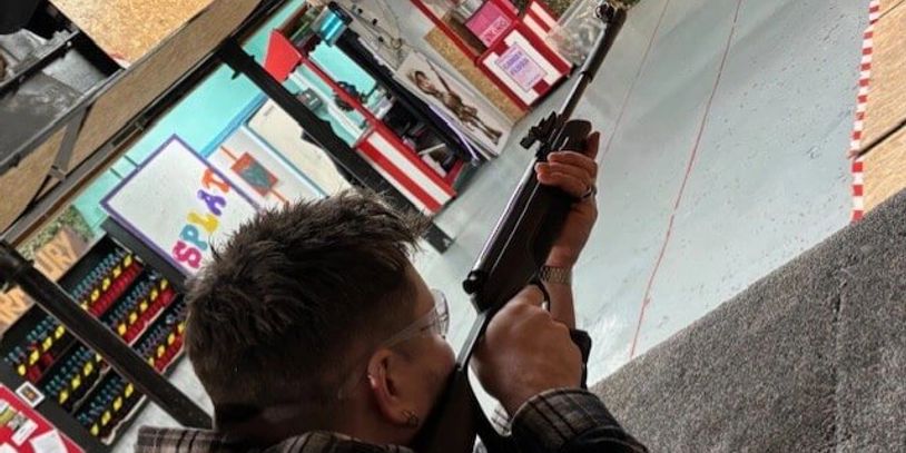 Person aiming a rifle at an indoor shooting range.