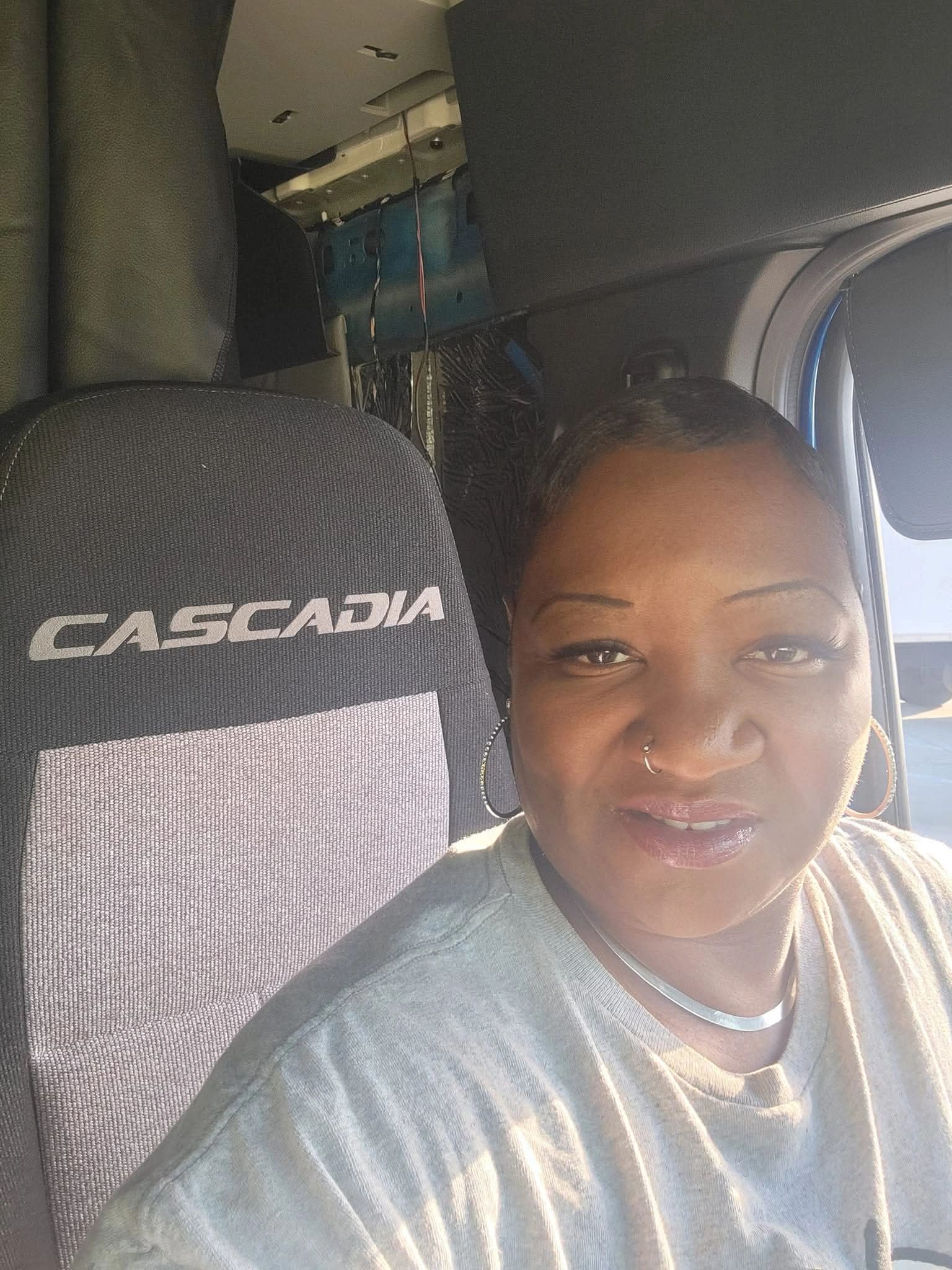 A woman taking a selfie inside a Cascadia truck cabin in sunlight.