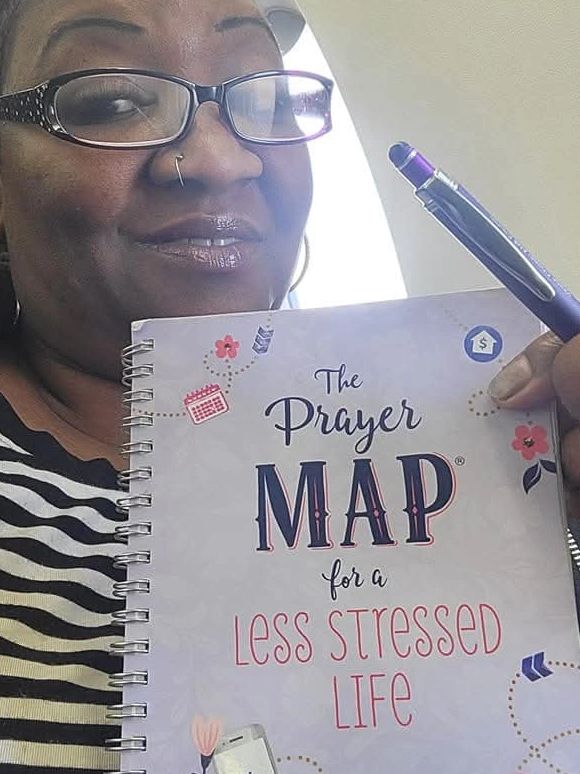 Woman holding a notebook titled 'The Prayer Map for a Less Stressed Life'.