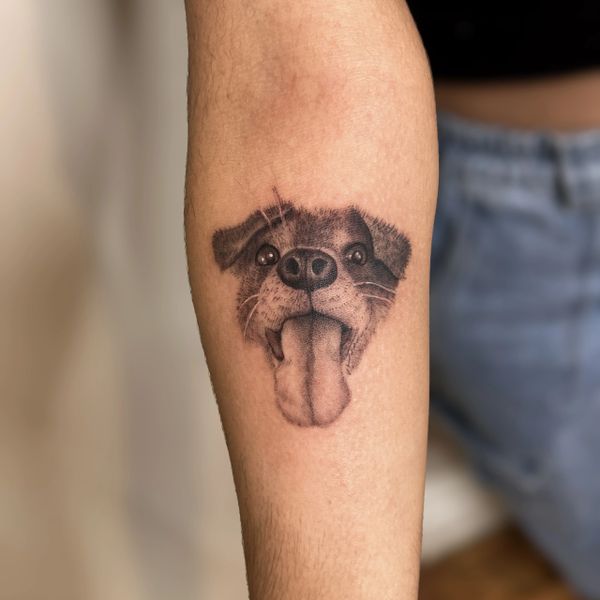 Tatuaje realista de la cara de un perro con la lengua afuera en el antebrazo.