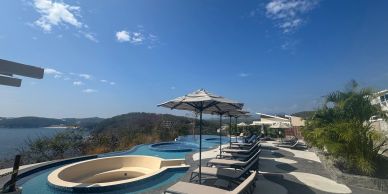 Swimming pools with lounge chairs and umbrellas on a sunny day.