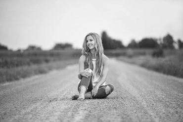 Young woman sitting barefoot on a rural gravel road.